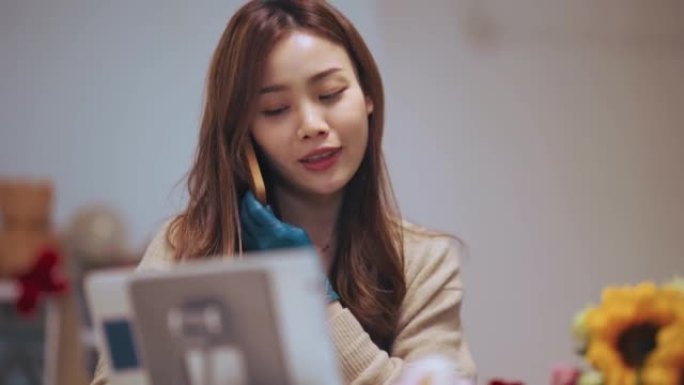 亚洲中国女花店，小企业花店老板，在工作场所在数字平板电脑上工作时在智能手机上聊天。检查股票，接受客户