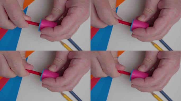 艺术家削尖红色铅笔，顶视图。一个男人用卷笔刀和铅笔的手的特写