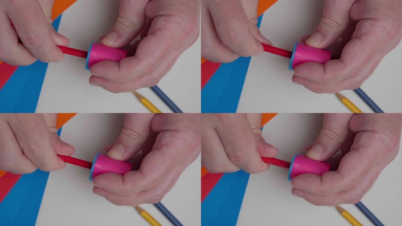 艺术家削尖红色铅笔，顶视图。一个男人用卷笔刀和铅笔的手的特写