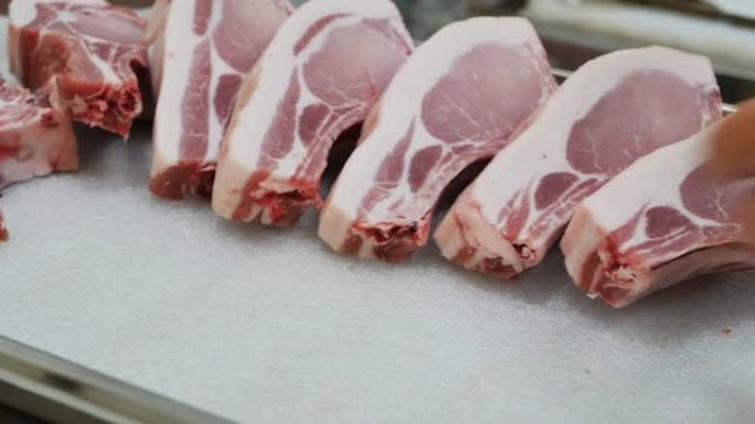 屠夫的手躺在托盘上，美丽的肉生了，边缘周围有一块脂肪。肉生牛排由屠夫放在基材上，从杂货店的窗户出售。