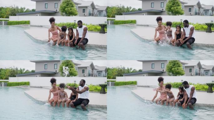 美国非裔家庭，肌肉发达的父亲，运动苗条的母亲和两个小孩正坐着，把腿放在水里。他们在游泳池边互相泼水，