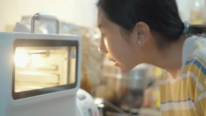 亚洲女孩打开烤箱，独自在家里的厨房里闻到自制烤鸡的味道，生活方式的概念。