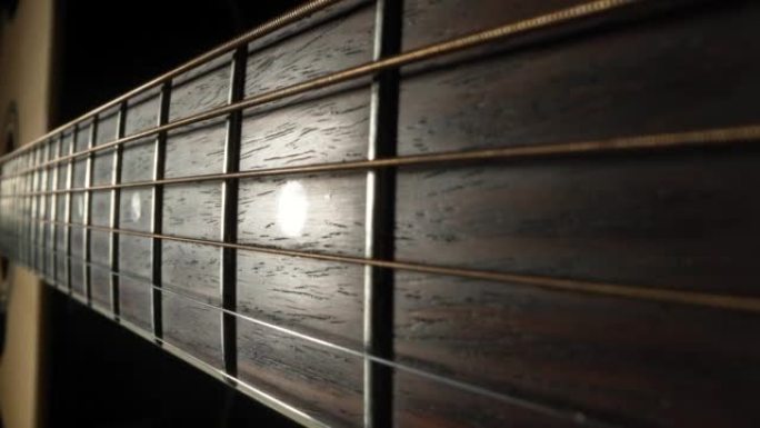 相机在黑色背景下平移古典原声吉他的指板。棕色木制吉他琴颈，金属琴弦和琴弦极端特写