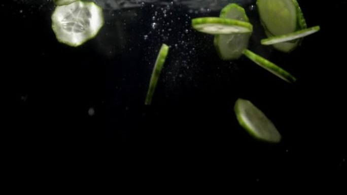 在黑色背景上，黄瓜碎片掉入水中。