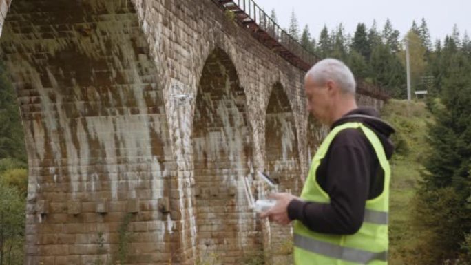 无人机在桥下进行检查。天桥旁边的无人机操作员。用于观察桥梁的四轴飞行器。道路和桥梁维护技术。无人机工
