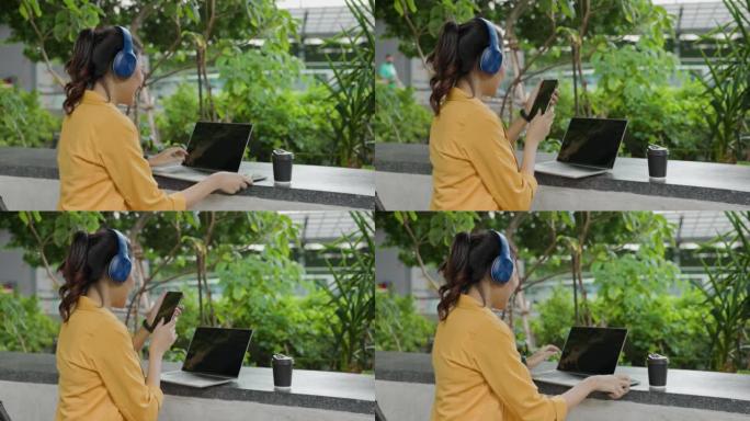亚洲女商人坐在蓝牙耳机在户外笔记本电脑上工作快乐的微笑。女士快乐地使用平板电脑公园。利用现代互联网通