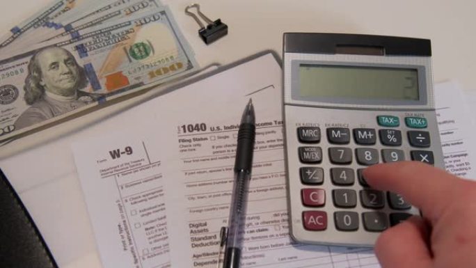 在计算器上计算金额1040和W9个人税单放在美国公民的办公桌上。