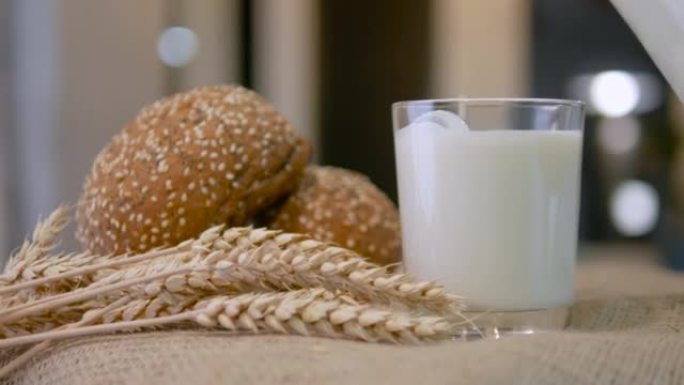 将牛奶从水罐倒入玻璃杯中。新鲜糕点配牛奶，乡村食品静物，小麦面包配牛奶。