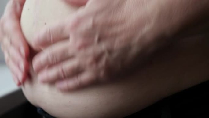 成熟的女人抚摸和挤压窗台附近的胖肚子