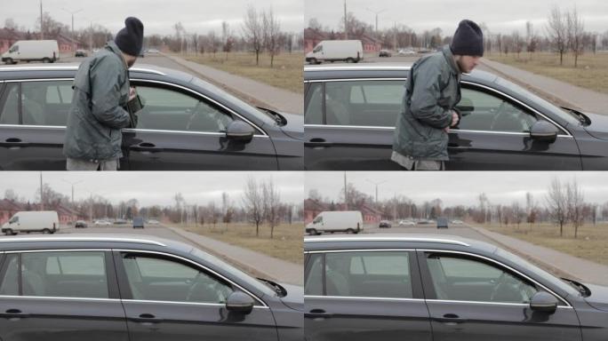 流浪汉在公共停车场走向一辆车，男窃盗从微微打开的车窗往外看，然后走开。带有报警系统的车辆。针对盗窃犯