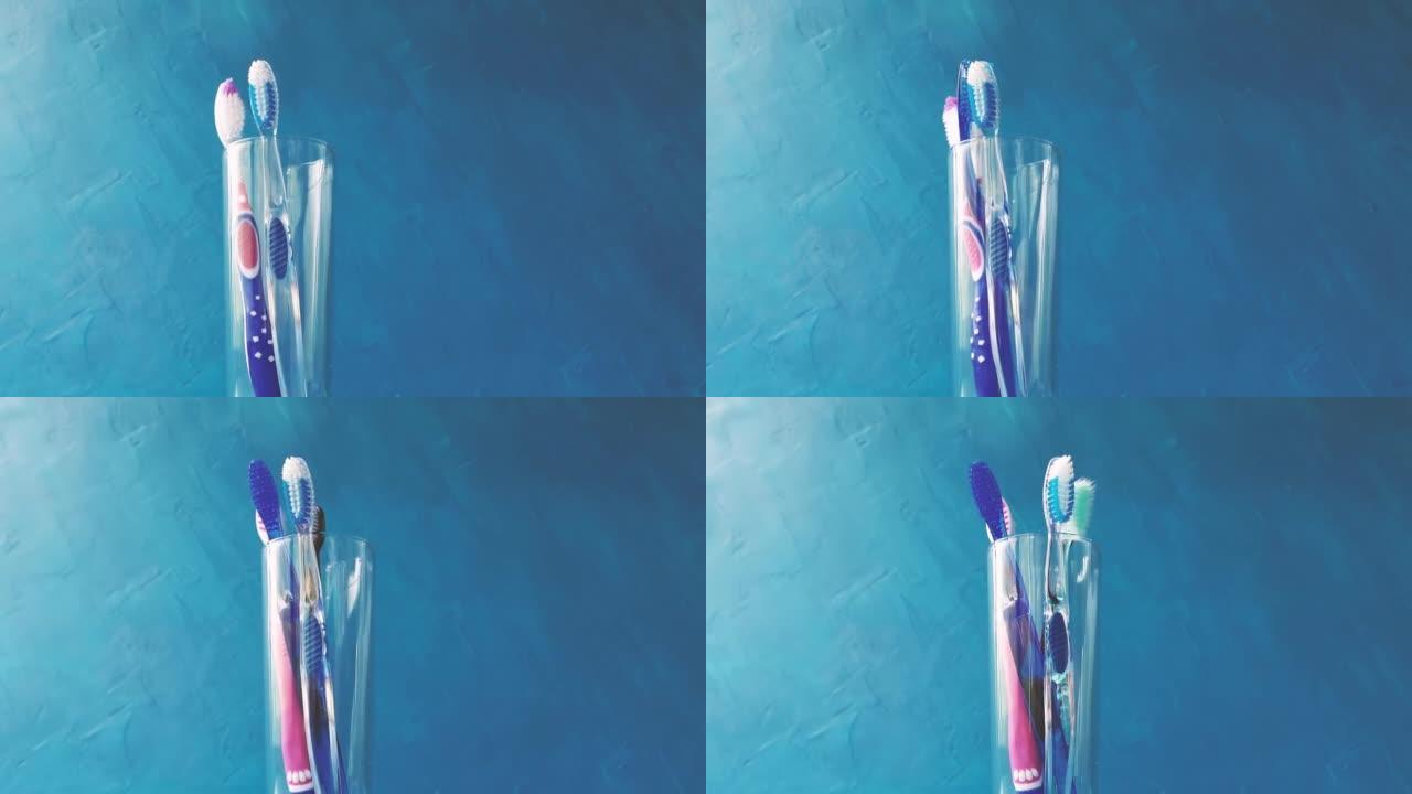 一只手将不同的多色牙刷放入蓝色背景上的玻璃特写镜头中。4k原始视频，摄像机运动流畅。