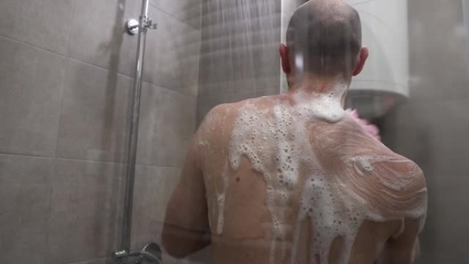 年轻的白种人男子用泡沫海绵洗澡的背影。特写镜头。日常卫生及皮肤护理