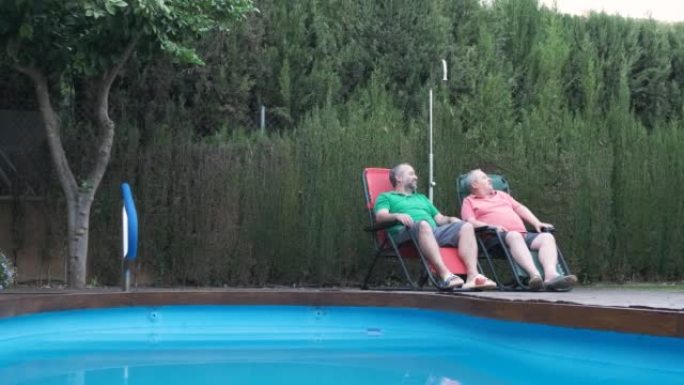 两个男人坐在游泳池附近的花园里放松身心，还有一条狗。