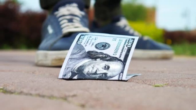 人行道上一百美元钞票的特写镜头，一个走路的人找到了它