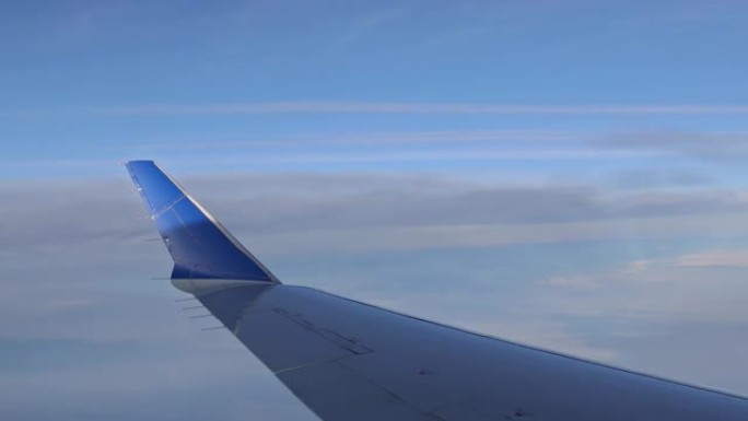 有趣的是，通过窗户看到飞机机翼在多云的天空上方飞行，背景是蓬松的云层