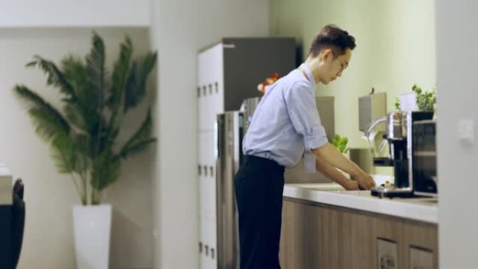 亚洲商人在餐具室洗他的可重复使用的杯子。
