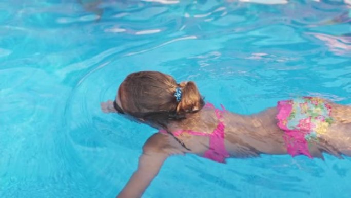 一个穿着明亮泳衣的女孩带着泳镜潜入透明水的游泳池