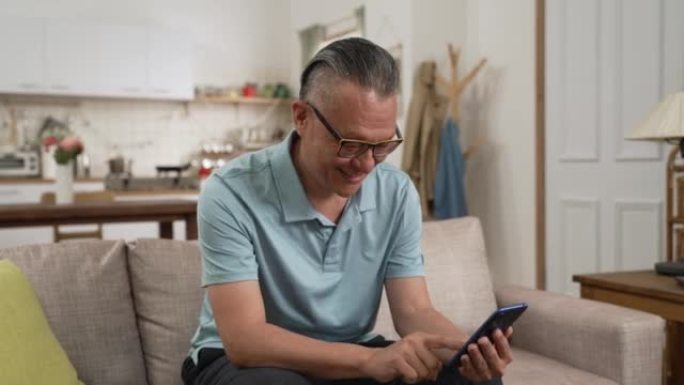 亚洲日本退休男子在家中客厅独自用手机阅读网络新闻的肖像