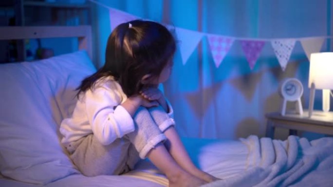 悲伤的小女孩在晚上睡觉前在黑暗的卧室里拥抱膝盖在床上哭泣，独自一人没有父母的概念
