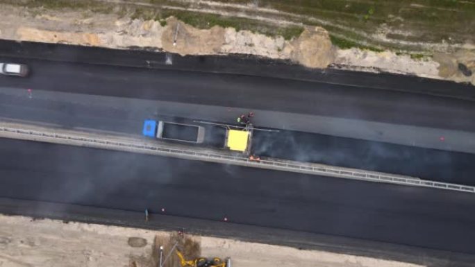 无人机向下移动到黄色道路摊铺机和工人。高速公路上的道路工程
