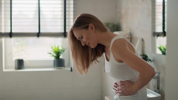年轻的白人妇女站在浴室里，感到胃部疼痛。用8k的红氦相机拍摄。