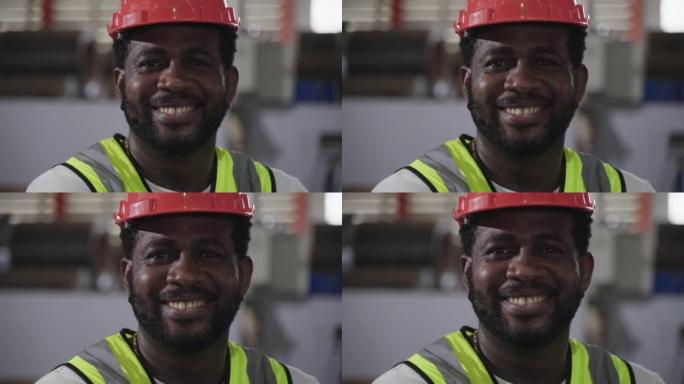 在工厂工业中，快乐的职业非裔美国男子工人的肖像戴着安全帽站着微笑，看着相机。