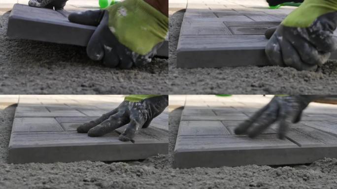 用铺路石铺路。一名戴着手套的建筑工人的手将铺路板放在沙子上，并用塑料绿色锤子敲打。户外特写。慢动作