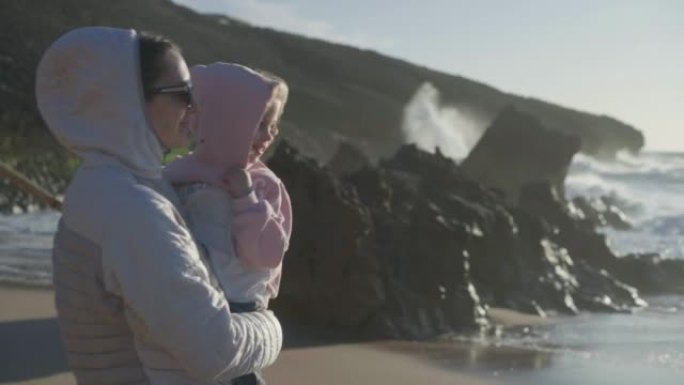 春天妈妈手捧孩子站在海边，穿着暖和的衣服手持视频效果