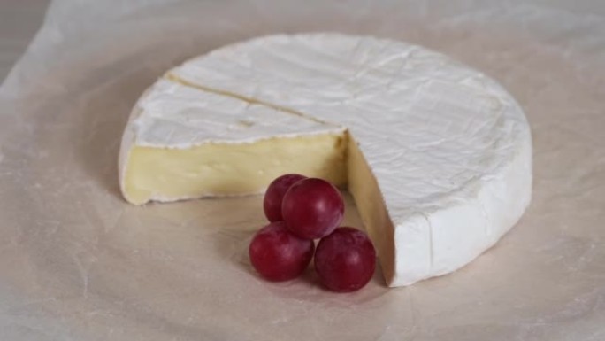 卡门培尔奶油奶酪和葡萄特写旋转。羊奶奶酪的头，木板上有白色霉菌。圆头卡门培尔切成块美味的软奶酪卡门培