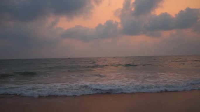 印度果阿坎多利姆海滩日落时海浪的广角慢镜头。日落时海面上的云。美丽的海滩日落背景。海滩概念的暑假。