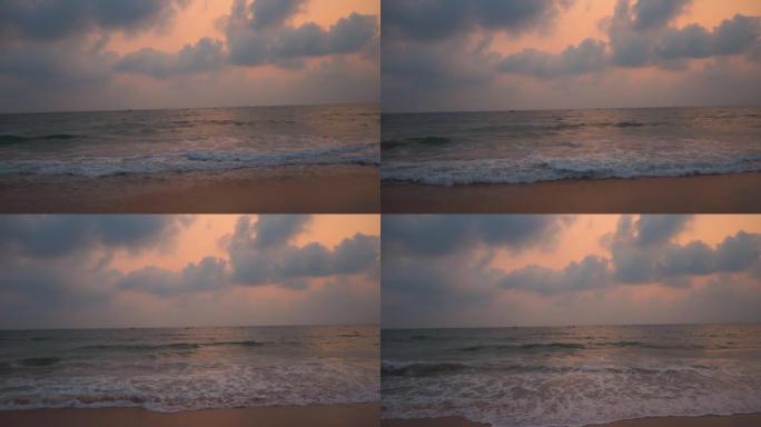 印度果阿坎多利姆海滩日落时海浪的广角慢镜头。日落时海面上的云。美丽的海滩日落背景。海滩概念的暑假。