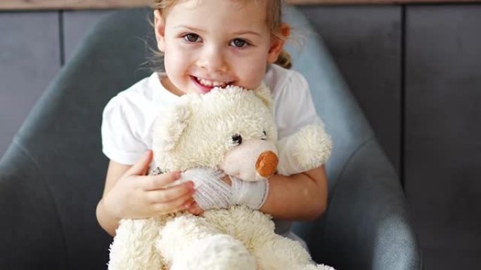 在医院的医生预约时，手指折断的小女孩抱着用绷带包扎的爪子的泰迪熊