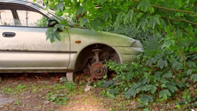 在垃圾场灌木丛中遗弃的砖块上没有轮子的汽车残骸