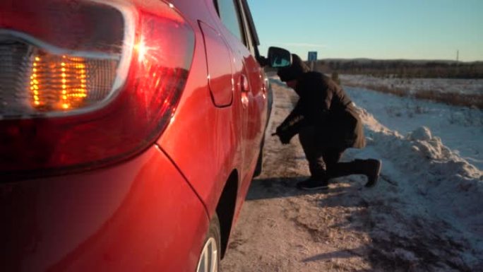 在阳光明媚的冬日，汽车在路边紧急停车。一个人在汽车上换了一个轮子。