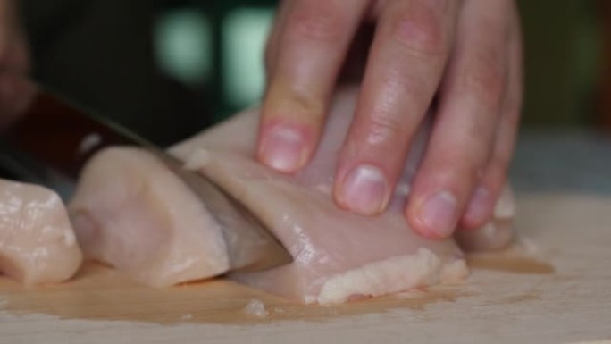 在切好的木板上关闭鸡柳。男人的手刀切片精致的火鸡鱼片在木制切板上。厨师切鸡胸肉，生白肉，厨师煮鸡胸肉