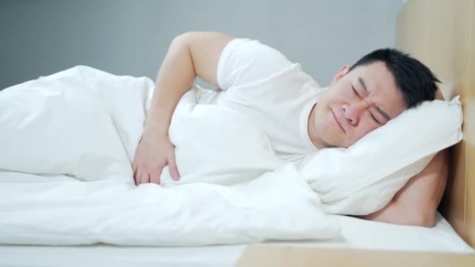 年轻患病的亚洲男子腹痛严重，胃痛中毒。早上躺在床上在家受苦