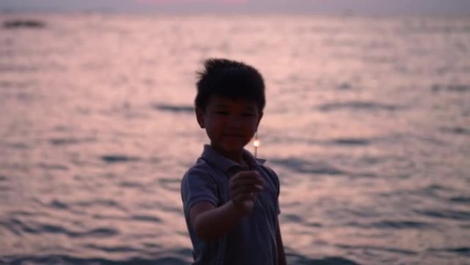 亚洲男孩晚上在海滩上玩烟火。庆祝的概念