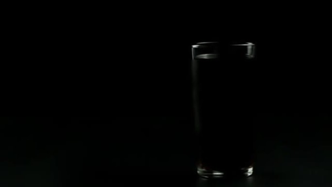 在黑色背景上装满黑色苏打水的玻璃杯，玻璃杯附近有水滴