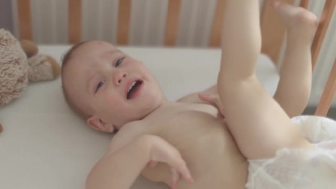 画像中哭着尖叫的裸婴婴儿，躺在婴儿床的摇篮里