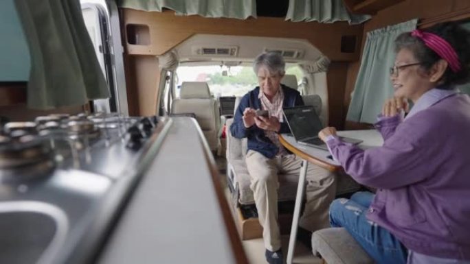 亚洲中国老年夫妇在房车内使用笔记本电脑和智能手机