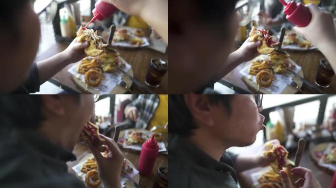 年轻人在汉堡上吃番茄酱，并在与朋友共进午餐时大口大口。