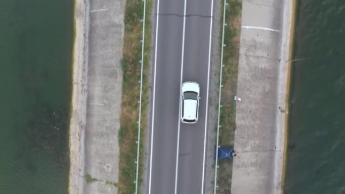 白色汽车穿过大坝路线的俯视图。夏季，SUV在湖附近的道路上行驶。飞越汽车穿过河桥或池塘。风景之路。旅