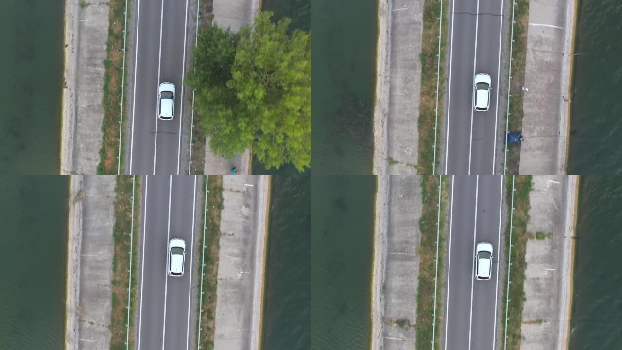 白色汽车穿过大坝路线的俯视图。夏季，SUV在湖附近的道路上行驶。飞越汽车穿过河桥或池塘。风景之路。旅