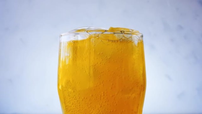白色墙壁背景上的冰立方特写玻璃中的橙色苏打水气泡。湿玻璃配流行橙色苏打水。4k宏原始视频60 fps
