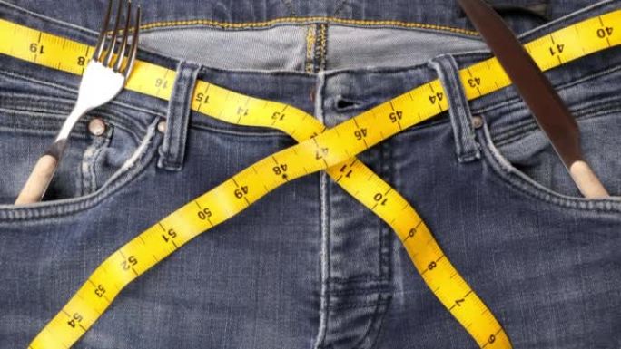 饮食和减肥概念。腰上的卷尺和牛仔裤口袋里的叉子和小刀作为饮食概念。健康的生活方式。健康食品。健康饮食