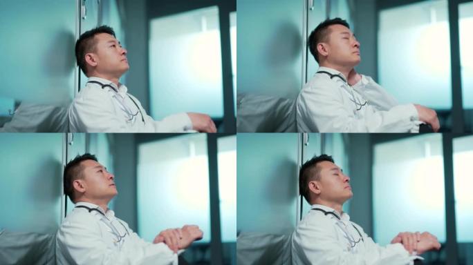 紧张疲惫的亚洲医生坐在医院的走廊里。疲倦沉思的医生在临床上悲伤的男性压力的医护人员
