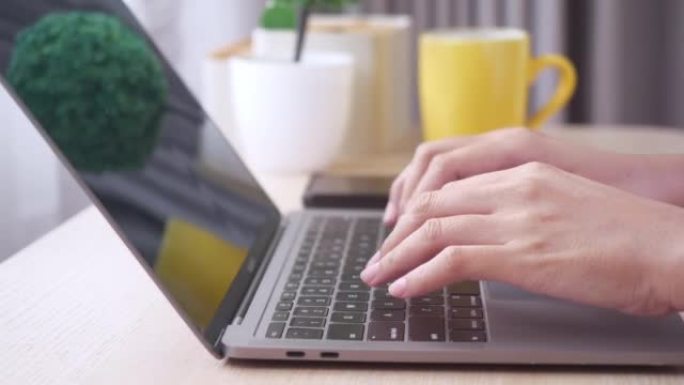 在家中在笔记本电脑键盘上打字的女性手的特写。
