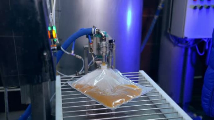透明塑料袋通过开口装满果汁。工厂工人将袋子弄平，以更好地填充果汁。