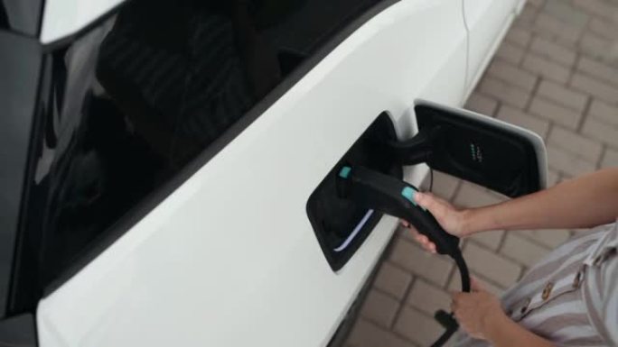 女人将充电器插入她的现代新型电动汽车的插座