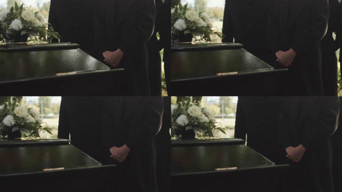 穿着黑色外套的人在户外葬礼上站在棺材旁